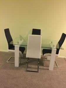 a glass dining room table with four white chairs at DatePalm CBD & Central Akl in Auckland