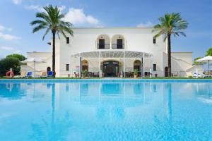 einem großen Pool vor einem Gebäude mit Palmen in der Unterkunft Tenuta La Baronessa Resort in Tuglie