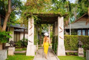 a woman in a yellow dress and a hat walking through an arch at Fisherman's Resort Haad Chao Samran in Haad Chao Samran