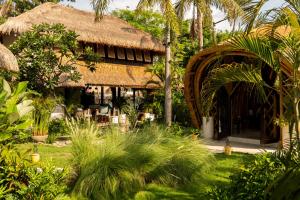 a house with a thatched roof in a garden at Villa Tokay - The Luxury Resort in Gili Islands