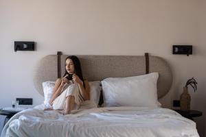 a woman sitting on a bed looking at her cell phone at VAYA Suites by Omilos Hotels in Amoudara Herakliou +42 photos