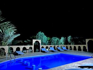 a swimming pool at night with lounge chairs around it at Auberge el oasis mharech in Foum Mharech