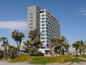 a tall white building with palm trees in front of it at Novotel Arica in Arica