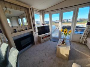 a living room with a television and a table with flowers at Lilly Luxury Hot Tub Caravan - theluxurycaravan - GV109 Grange Leisure Park in Mablethorpe