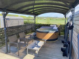 a hot tub on a deck with chairs and a table at Highland Gateway Glamping in Clackmannan
