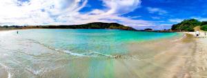 a beach with turquoise water and people walking on it at Seascape Peninsula Bach in Kaitaia