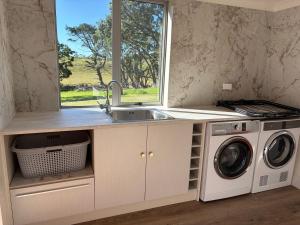 a kitchen with a sink and a washing machine at Pouto Farms Packhouse - Coastal Farmhouse in Pouto