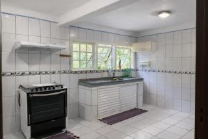 a white tiled kitchen with a stove and a sink at Pouso Ravenala - Refúgio do viajante in Paraty