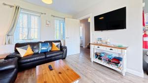 a living room with a black leather couch and a flat screen tv at Nantucket Cottage - Part of the The Bay Filey Holiday Village with pool, gym and direct beach access, pub, restaurant, tennis and meadows walks in Filey