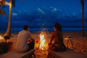 a man and woman sitting around a fire on the beach at Petit Lafitte Beach Front Hotel & Bungalows in Playa del Carmen