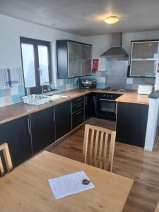 a kitchen with black cabinets and a wooden table at Harbour Views, Coverack in Helston