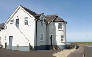 a white house with the ocean in the background at SeaBreeze - Portballintrae in Portballintrae