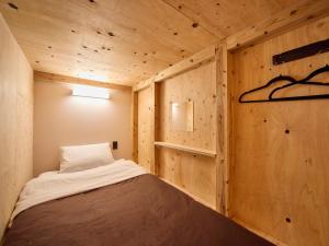 a small bed in a room with wooden walls at Southern Gate HIVE in Ishigaki Island