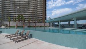 a swimming pool with two chairs and a large building at Beachfront Luxury Studio in Puerto Peñasco