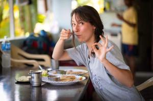 a woman sitting at a table eating food with a fork at Hampi Banana Farm House in Hospet