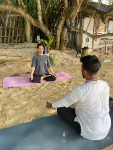 a man and woman sitting in a yoga pose on the beach at Serene Garden Lodge in Ahangama