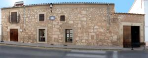 a stone building with two doors and a street at Casa Rural La Chimenea in Navas del Madroño