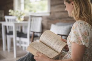 a woman sitting on a couch reading a book at Smålandstorpets lanthotell in Hok