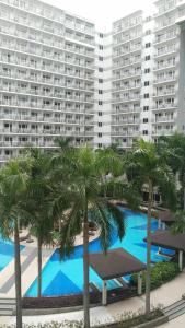 a pool with palm trees in front of a large building at Nygel Staycation at Shell Residences in Sampong