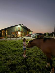a little girl feeding a horse in front of a barn at Rancho Mavi Hospedagem Colônia Witmarsum in Palmeira