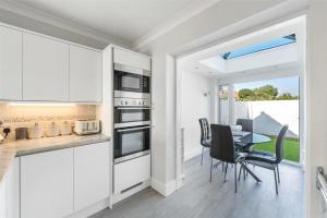 a kitchen with white cabinets and a table with chairs at Ocean View in Worthing, 5 bedrooms for 10, 3 Bathrooms, Hot Tub, Parking for 6, Seaview in Sompting