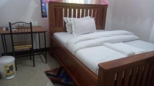 a bed with a wooden frame with a pillow and a table at GcAnnexLodge in Iringa