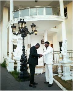 two men shaking hands in front of a building at The Peacock Mansion in Kumasi