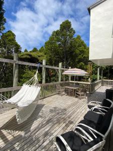 a hammock on a deck with chairs and a table at Kauri Coast Bungalow in Karekare