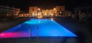 a large blue swimming pool at night with lights at riad tighmart in Merzouga