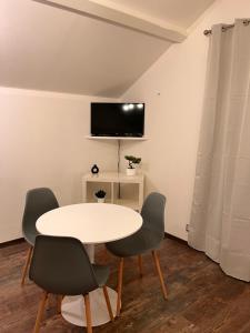 a white table with four chairs and a tv on a wall at L'escale Aéro Lyon in Saint-Laurent-de-Mure
