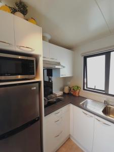 a kitchen with white cabinets and a black microwave at Puriri Tiny Home in Orewa