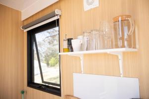 a kitchen with a shelf with glasses and a window at Beckford Tiny House 2 by Tiny Away in Good Hope