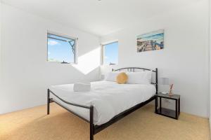 a white bedroom with a bed and two windows at ParkView on Owen in Huskisson