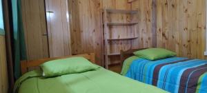 two beds in a room with wooden walls at Alojamiento Los Canelos in Ancud