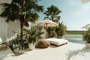 a patio with a white couch and an umbrella and palm trees at The Iggy Villa 2BR in Cemagi
