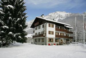 a large building in the snow next to a tree at Meublè Cima Bianca Garni in Bormio