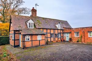 an old brick house with a driveway in front of it at Cricketers cottage in Tirley
