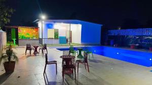a patio with chairs and tables and a pool at night at Drop Hills Farm Noida in Noida