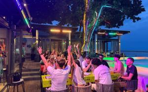 a group of people sitting at a table with their hands in the air at Lub d Koh Samui Chaweng Beach - Beachfront & Vibrant Social Vibe in Chaweng