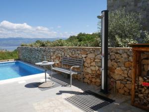 a bench next to a stone wall next to a swimming pool at Villa Paradise in Vrbnik