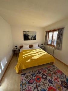 a bedroom with a bed with a yellow blanket and a rug at Waldheim Laax Pension in Laax