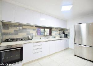 a kitchen with white cabinets and a stainless steel refrigerator at קסם הרימון - 4 צימרים מושלמים עם בריכה וג'קוזי in ‘Azriqam