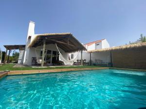 a villa with a swimming pool in front of a house at Pego Beach House in Grândola