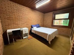 a bedroom with a bed and a desk and a brick wall at Quarto confortável no Centro in Botucatu