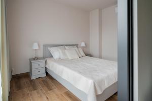 a white bedroom with a bed and a night stand at Apartamenty Szelągowskiej in Raszyn
