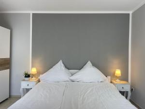 a white bed with white pillows and two lamps at Apartment Pangani Teichhof Fehmarn in Wenkendorf