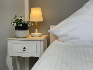 a bedside table with a lamp and a white bed at Apartment Pangani Teichhof Fehmarn in Wenkendorf