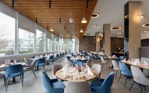 a dining room with tables and chairs and windows at Hunguest Hotel Apollo in Hajdúszoboszló
