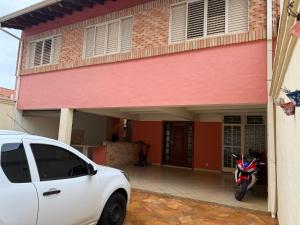 a white car parked in front of a house with a motorcycle at Quarto em ótima localização in Botucatu