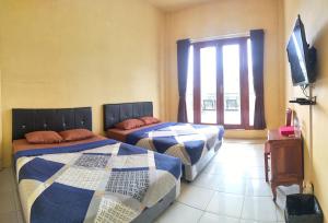 two beds in a room with a tv and a window at Hotel Nur Cahaya - Syariah in Probolinggo